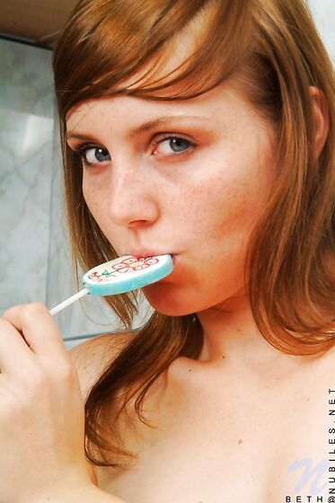 Red Haired Teen Babe Beth Nubiles Slowly Strips While Eating A Lollipop.